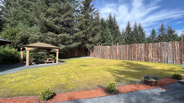 A backyard with a wooden pergola, a wooden fence, and a well-maintained lawn.