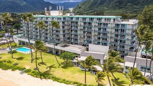 Un hotel de varios pisos con piscina, rodeado de palmeras y montañas.
