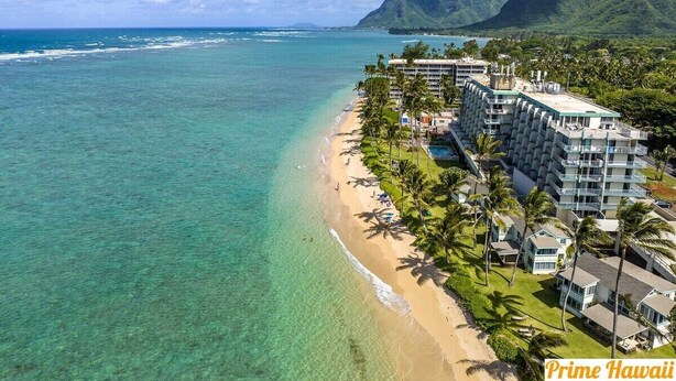 Un hotel frente a la playa con varios pisos, una piscina y vistas al océano y a las montañas.