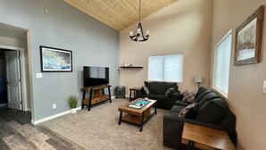A living room with a TV, sofa, coffee table, and a chandelier.