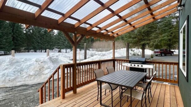 A wooden deck with a grill and table, surrounded by snow.