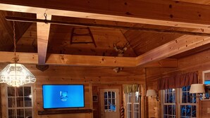 L’intérieur chaleureux d’un chalet avec une table à manger en bois, des chaises, un canapé en cuir, un téléviseur et une cheminée.