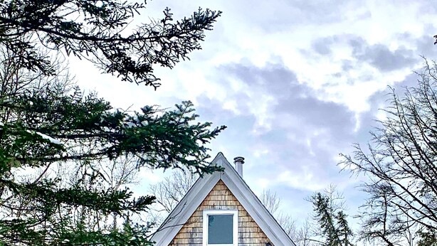 Une cabane en bois dotée d’un balcon, d’une porte rouge et d’une cheminée.