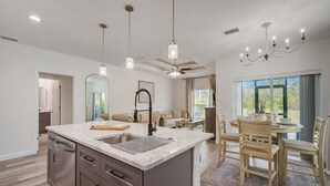 A modern kitchen with a central island, pendant lights, and a dining area with a table and chairs. - South West Family Home , 3 Bedroom 2 Bath, King bed suite, 4 Beds , 6 Guests  (Rotonda West)