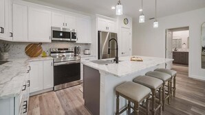 A modern kitchen with white cabinetry, stainless steel appliances, and a marble island with bar stools. - South West Family Home , 3 Bedroom 2 Bath, King bed suite, 4 Beds , 6 Guests  (Rotonda West)