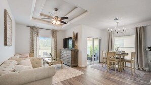 A spacious living room with a sofa, coffee table, and a TV on a wooden cabinet. There is a dining area with a table and chairs, and a ceiling fan above. - South West Family Home , 3 Bedroom 2 Bath, King bed suite, 4 Beds , 6 Guests  (Rotonda West)