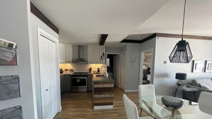 A modern kitchen with white cabinets, a stainless steel oven, and a wooden dining table with white chairs. - Ski in/ Ski out Modern 1 bedroom with fireplace (Mont-Tremblant)