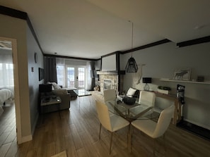 A modern living room with a glass dining table, a sofa, and a fireplace. - Ski in/ Ski out Modern 1 bedroom with fireplace (Mont-Tremblant)