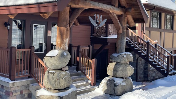 A lodge with a stone staircase, wooden railings, and a snow-covered roof. - Ski in/ Ski out Modern 1 bedroom with fireplace (Mont-Tremblant)