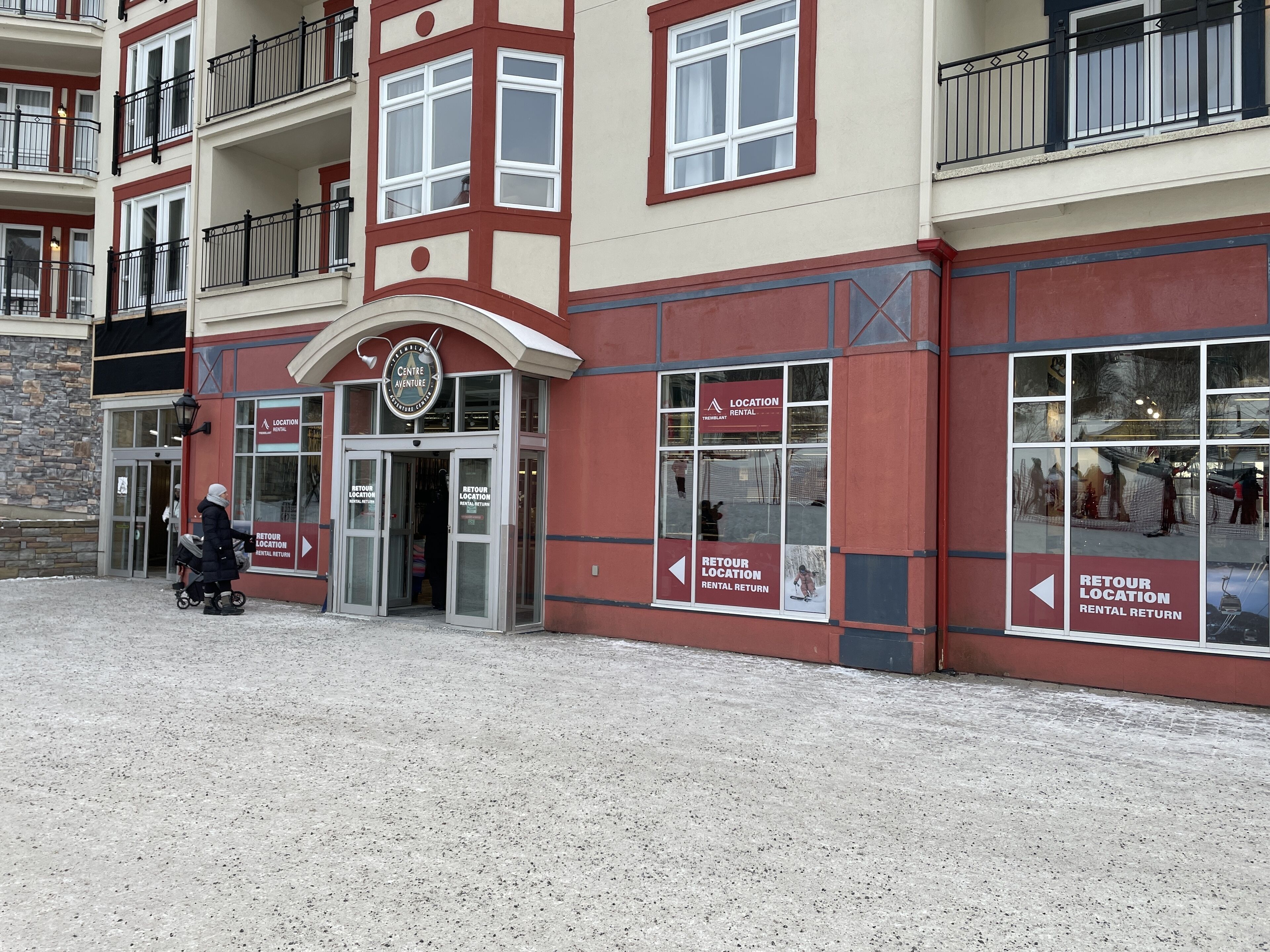 A multi-story building with a red and beige facade, a glass entrance, and signs indicating a rental location.