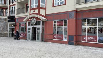 A multi-story building with a red and beige facade, a glass entrance, and signs indicating a rental location.