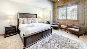 A bedroom with a large bed, wooden walls, a ceiling fan, and a view of a house through a window. - Gondola Vista 4 Bedroom Villa w/ Hot Tub (South Lake Tahoe)