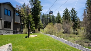 A modern building with a stone foundation, a well-maintained lawn, and a cable car in the background. - Gondola Vista 4 Bedroom Villa w/ Hot Tub (South Lake Tahoe)