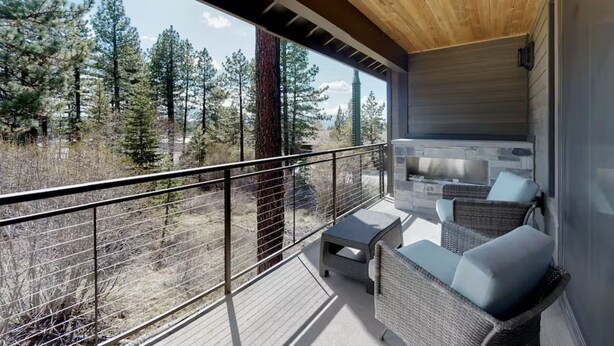 A balcony with wicker furniture and a stone fireplace, overlooking a forested area. - Gondola Vista 4 Bedroom Villa w/ Hot Tub (South Lake Tahoe)