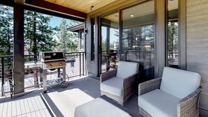 Una terraza al aire libre con una parrilla, sillas de mimbre y un ventanal que da a un patio.