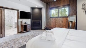 Un dormitorio con una cama grande, chimenea, televisión y ventana con vistas a árboles.