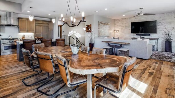 Una cocina moderna con armarios de madera, estufa integrada y comedor con una gran mesa de madera y sillas de cuero.