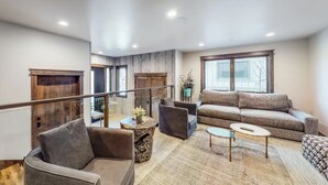 Un vaste espace de vie comprenant un canapé, des fauteuils et une table basse. Un escalier mène à l’étage supérieur.