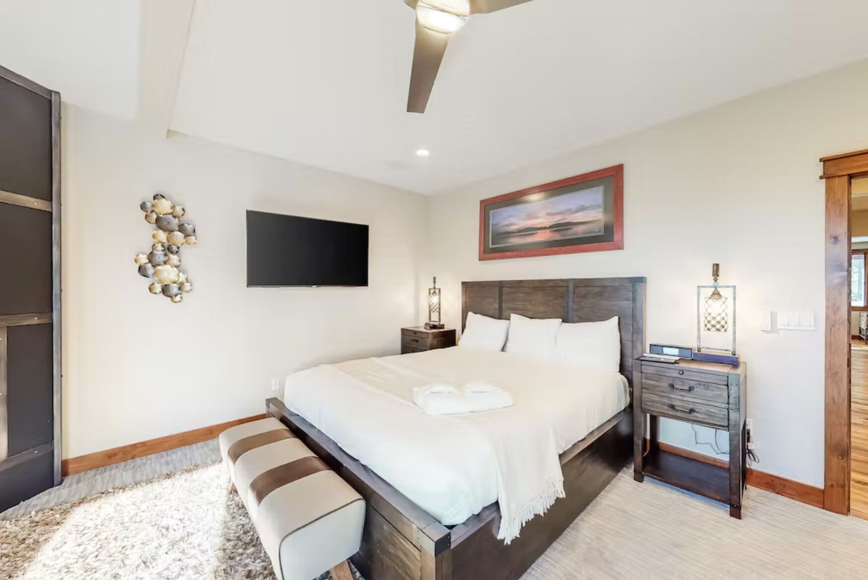 A modern bedroom with a large bed, a flat-screen TV, a painting, and a wooden nightstand.