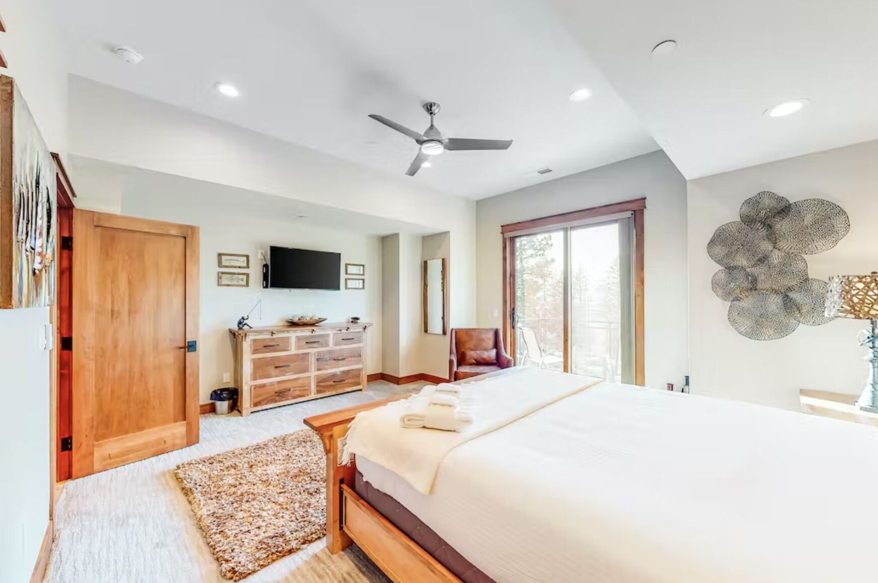 Une chambre avec un grand lit, une commode en bois, un ventilateur de plafond et une porte-fenêtre coulissante donnant sur un balcon.