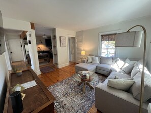 A living room with a sofa, coffee table, and lamp. There is a door leading to another room.