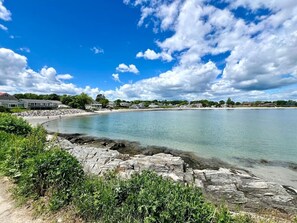 A coastal landscape with a clear sky, a sandy beach, and rocky shoreline.