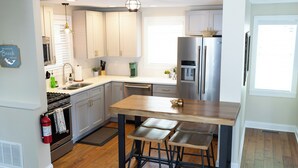 A modern kitchen with white cabinets, a stainless steel refrigerator, and a wooden island with bar stools.