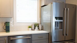 A kitchen with a stainless steel refrigerator, a built-in water dispenser, and a window with blinds.
