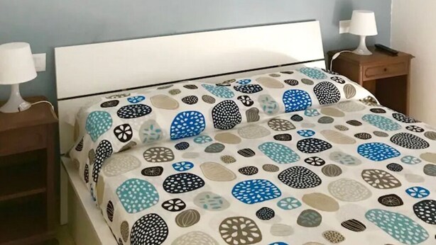 A bedroom with a bed, a nightstand, a lamp, and a wall with a beach-themed artwork. - Bright, renovated apartment with two bedrooms and parking space - 300m from the sea (Grado)
