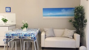 A dining area with a table set for four, a sofa, and a painting of a seascape on the wall. - Bright, renovated apartment with two bedrooms and parking space - 300m from the sea (Grado)