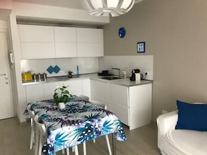 Um espaço compacto com cozinha compacta, área de refeições com mesa e cadeiras, e cama com travesseiro azul.