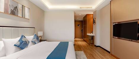 Habitación de hotel con una cama grande, televisión, suelo de madera y un cuadro en la pared.
