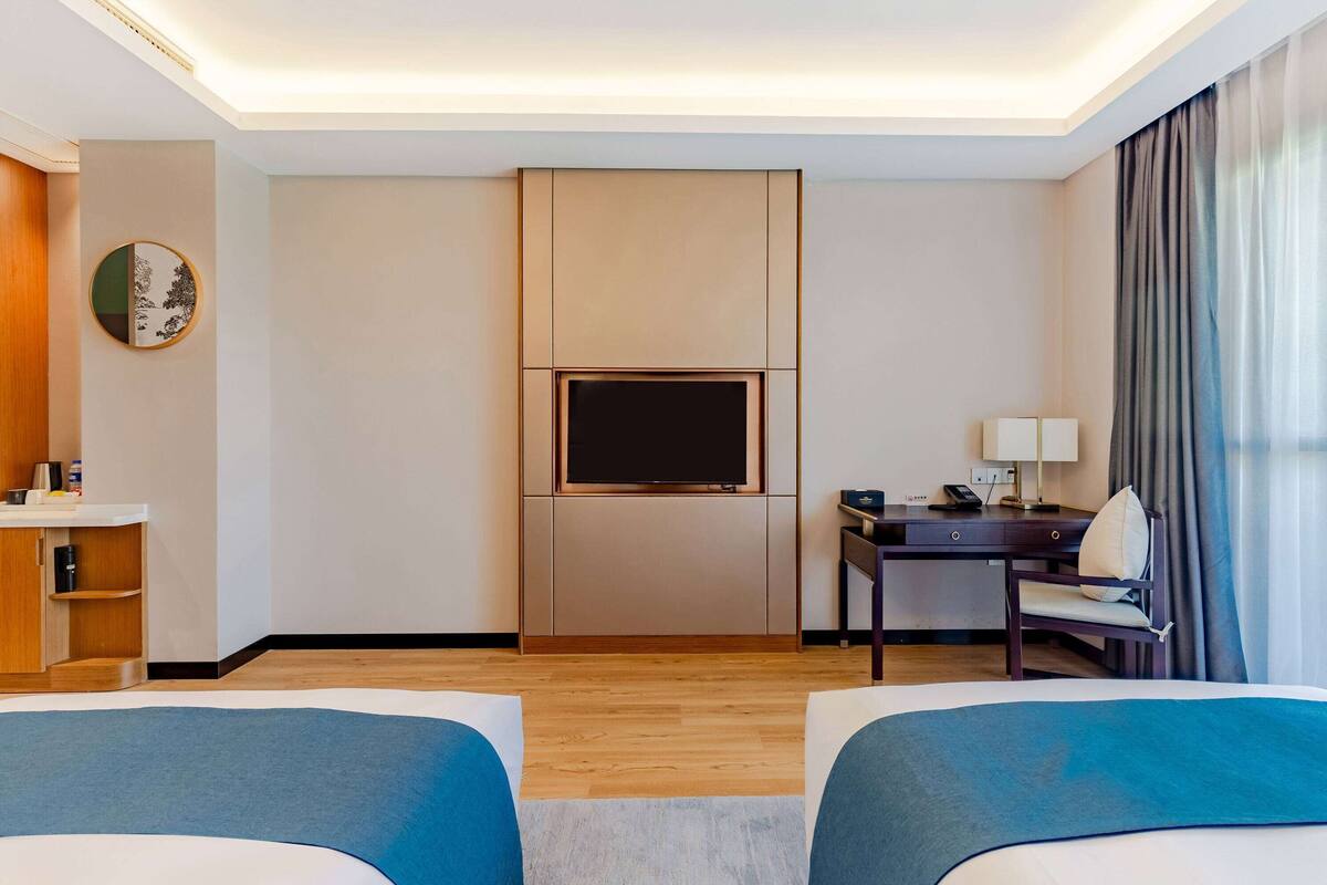 Une chambre d’hôtel avec deux lits, un bureau avec une lampe, un téléviseur à écran plat et une armoire en bois.