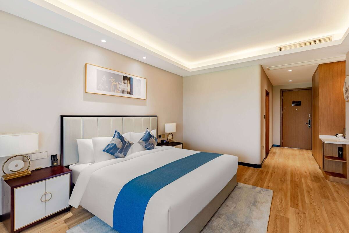 Une chambre d’hôtel avec un grand lit, des tables de chevet, un tableau encadré au mur et un plancher en bois.