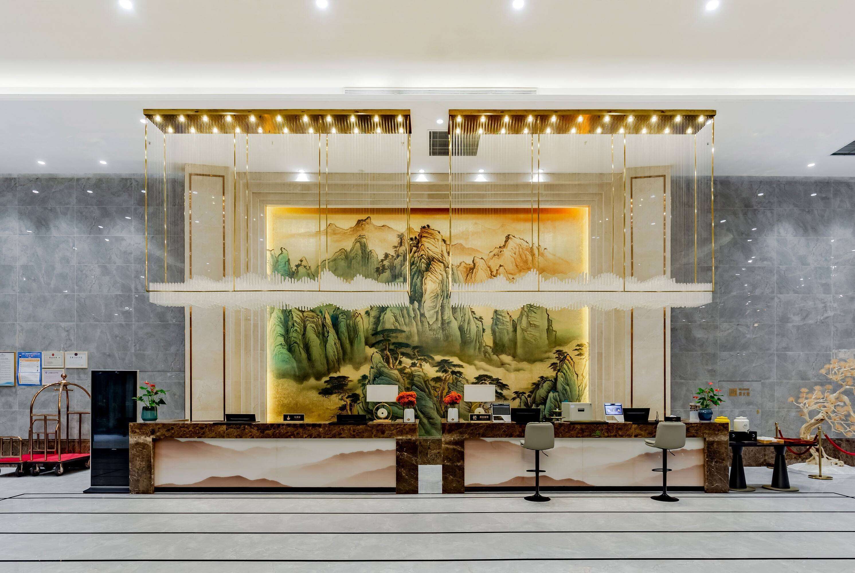 A hotel reception area with a large mural of mountains and trees, a reception desk with chairs, and a modern chandelier.