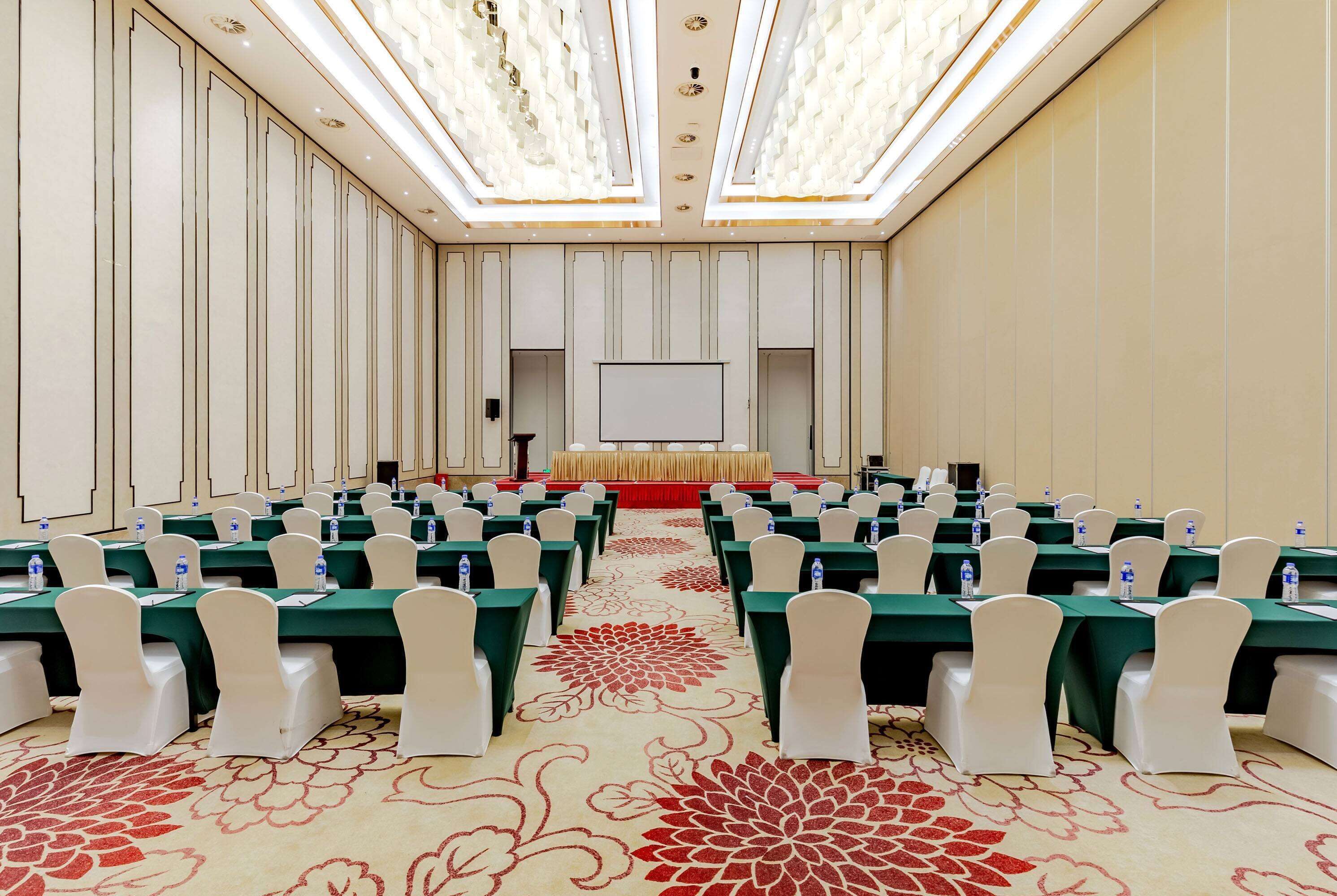 A conference room with rows of tables, white chairs, and a stage at the front.
