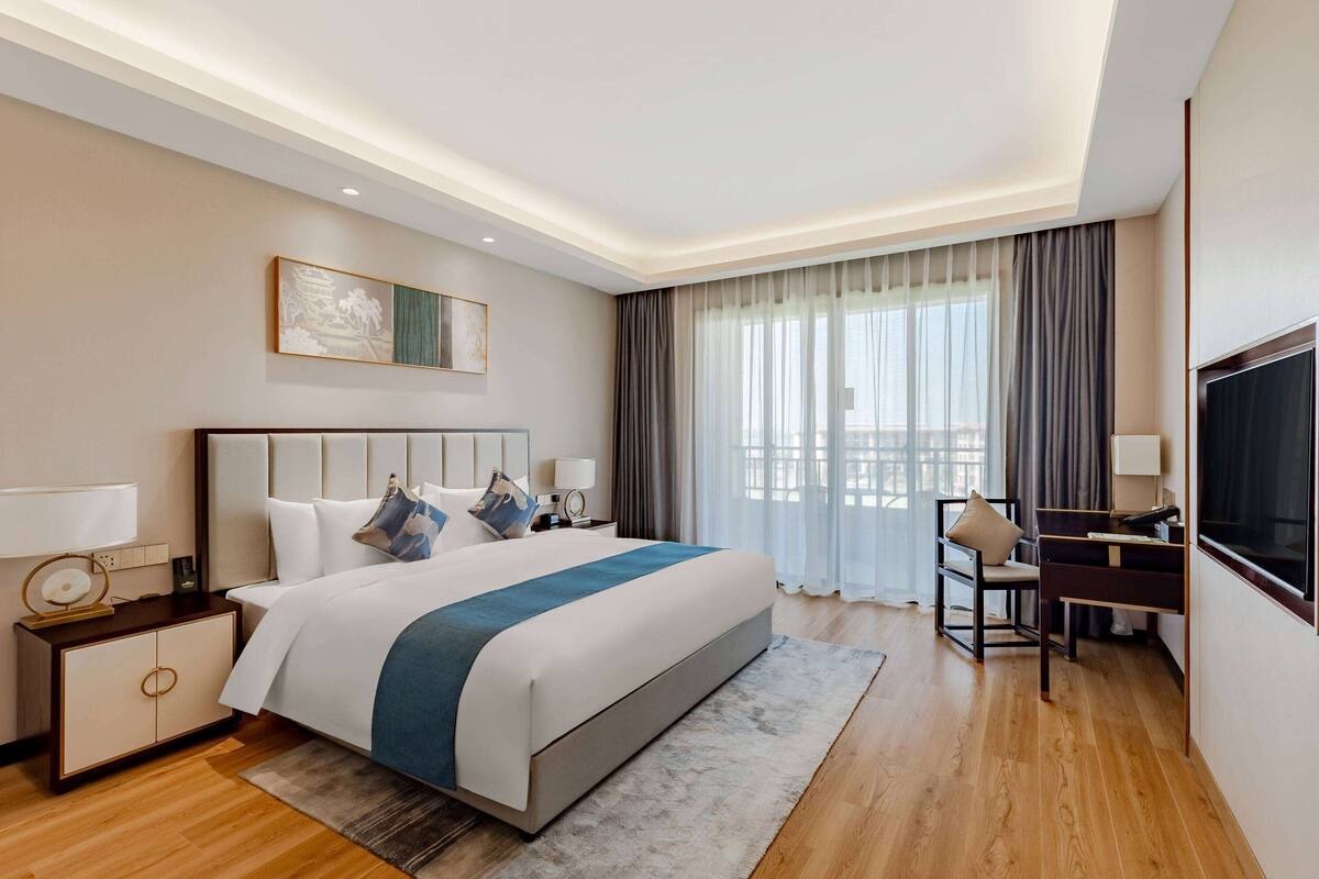 Une chambre d’hôtel avec un grand lit, un bureau, une télévision et une fenêtre avec des rideaux.