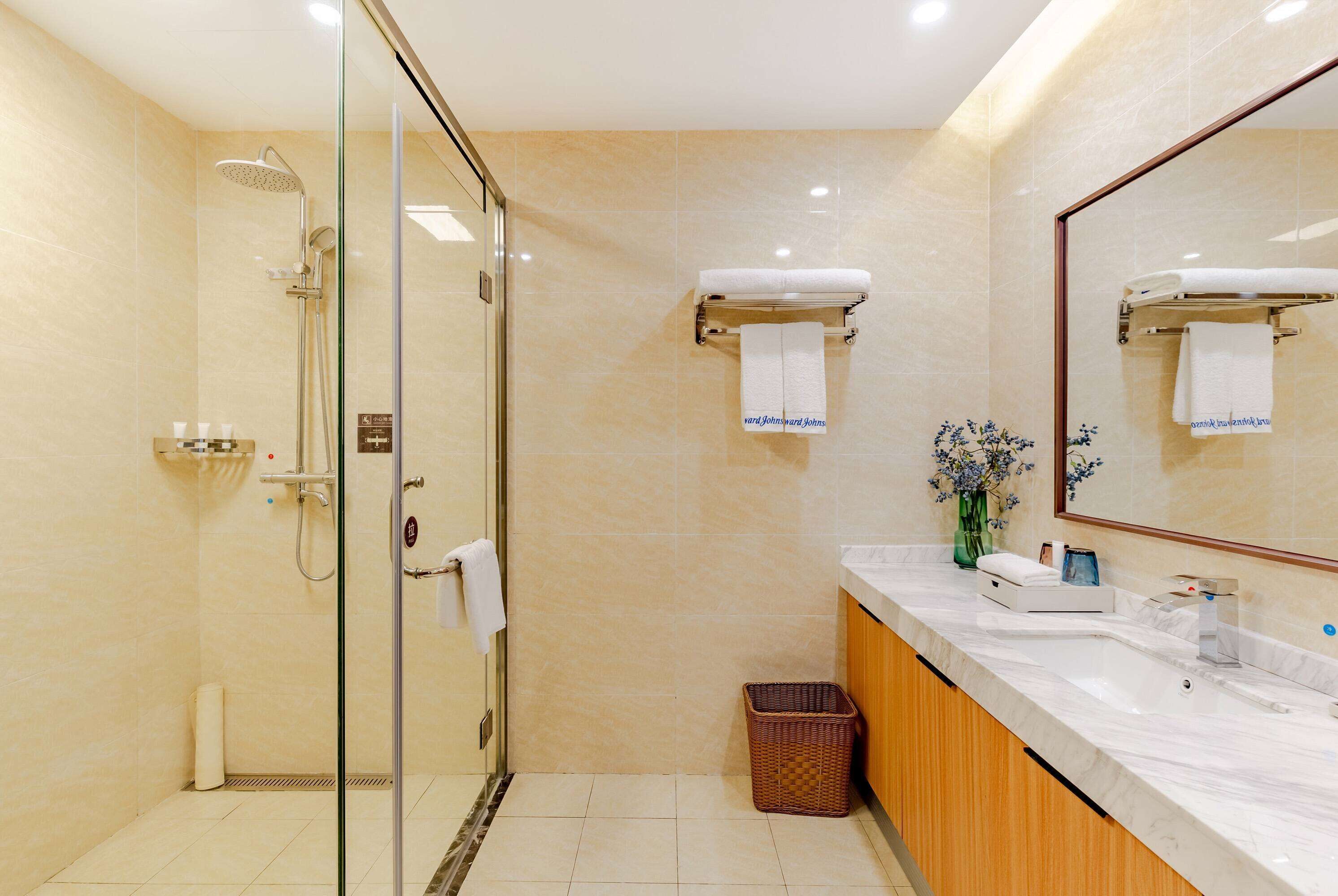 Un baño moderno con ducha envuelta en vidrio, tocador de mármol y un espejo grande.