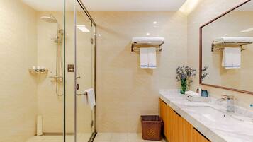 Un baño moderno con ducha envuelta en vidrio, tocador de mármol y un espejo grande.