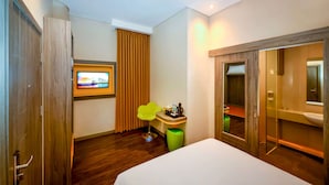 A hotel room with a wooden wardrobe, a small desk with a chair, a television mounted on the wall, and a bathroom with a mirror and sink. - Super 8 By Wyndham Solo Indonesia (Surakarta)
