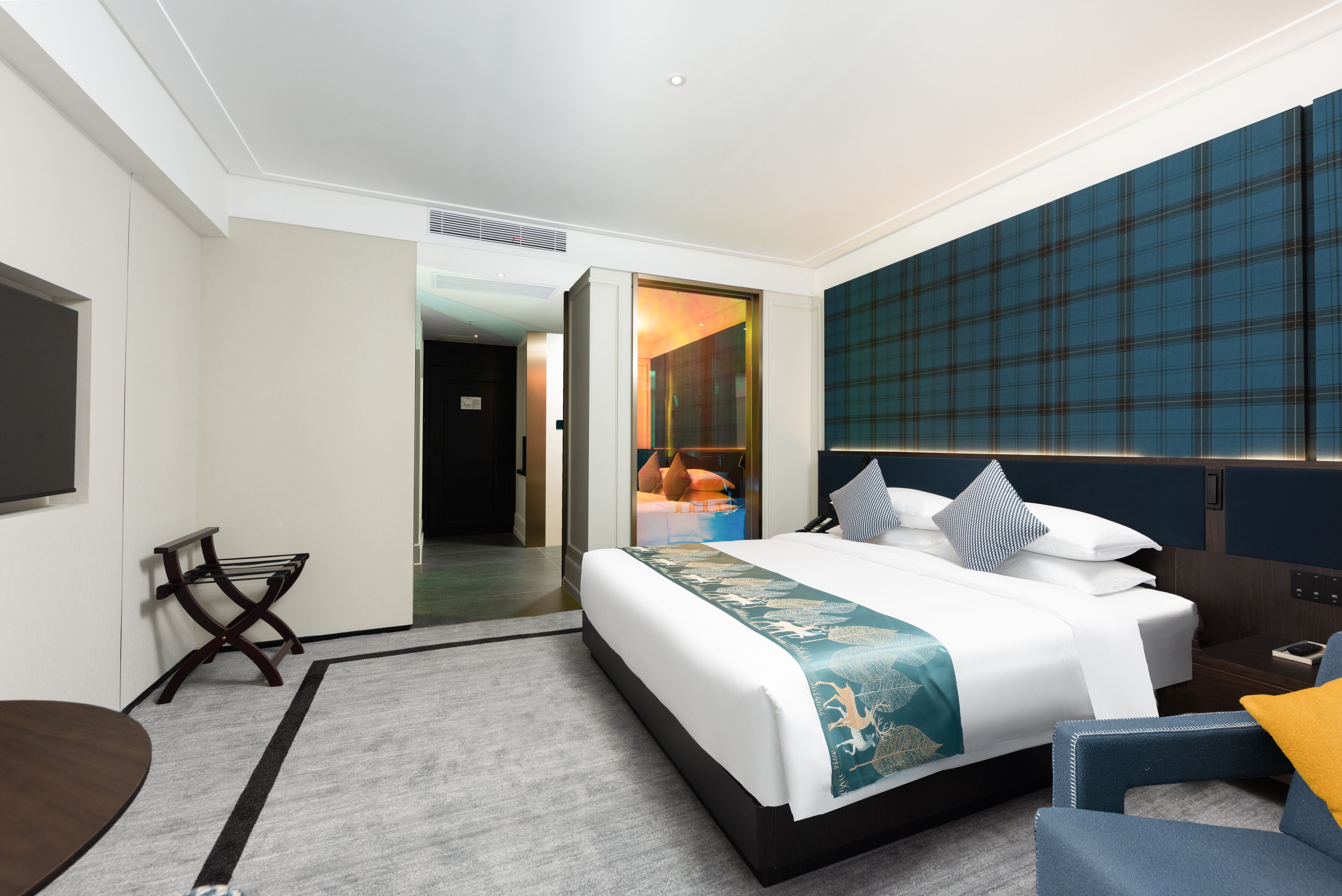 Ein Hotelzimmer mit einem großen Bett, einem Schreibtisch und einem Stuhl. Eine Tür führt in einen weiteren Raum.