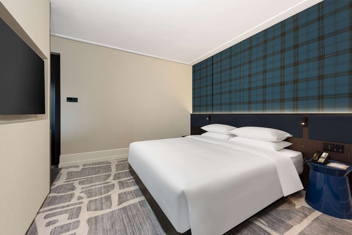 Ett hotellrum med en stor säng, en platt-TV som är monterad på väggen, en blå accentvägg och en mönstrad matta.