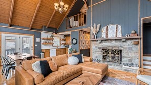 A cozy living room with a wooden ceiling, a stone fireplace, and a modern sofa. - Spacious Mountain Cabin for 8 (Deep Gap, Watauga County)