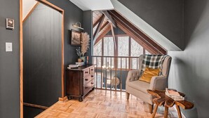 A room with a sloped ceiling, a wooden floor, a sofa, a side table, and a dresser. - Spacious Mountain Cabin for 8 (Deep Gap, Watauga County)