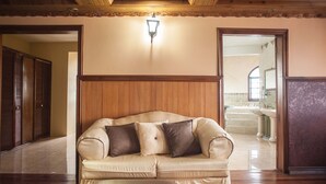 Een woonkamer met een beige bank, een houten plafond en een gang die naar een badkamer leidt.