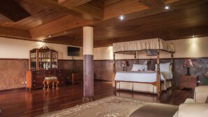 Een ruime slaapkamer met een hemelbed, houten vloeren, een grote spiegel en een klassieke ladenkast.