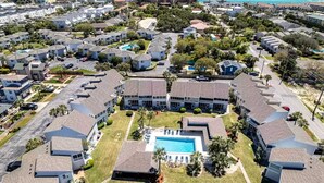 An aerial view of a residential area with multiple houses, a central building with a swimming pool, and a beach in the background. - Modern Coastal 2BR: Walk to Beach, Pool at Back Door (Destin)