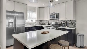 A modern kitchen with stainless steel appliances, a central island, pendant lighting, and a patterned backsplash. - Modern Coastal 2BR: Walk to Beach, Pool at Back Door (Destin)