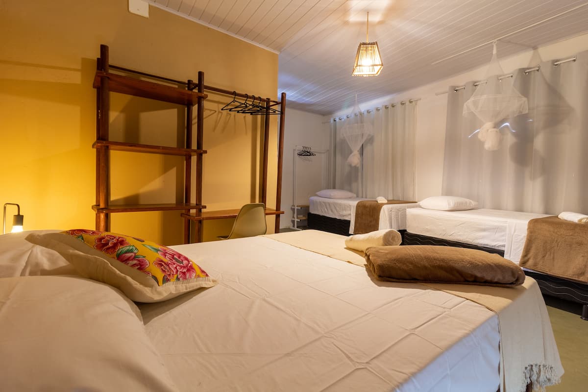 Quarto de hotel com duas camas, uma escada de madeira, uma escrivaninha e uma cadeira.