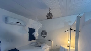 A hotel room with a bed, a bedside table, a hanging light fixture, a wall-mounted air conditioner, and a wall decoration. - Pousada Recanto da Mata (Porto Seguro)